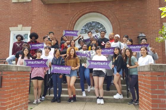 Photo of a group of international students on Chatham's campus, holding Chatham University signs.