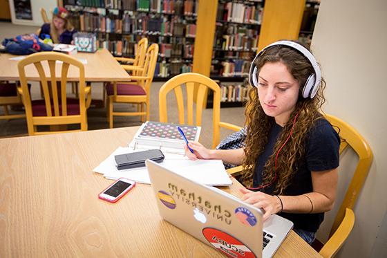 波胆网站的学生坐在珍妮·金·梅隆图书馆, 戴着耳机坐在桌子上学习，在电脑前工作. 