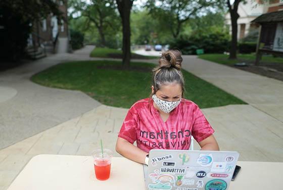 一名蒙面女学生身穿波胆网站衬衫的照片, 在足球波胆平台外用笔记本电脑工作