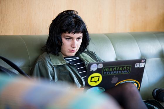图为一位波胆网站的女学生坐在图书馆的沙发上, 在笔记本电脑上工作