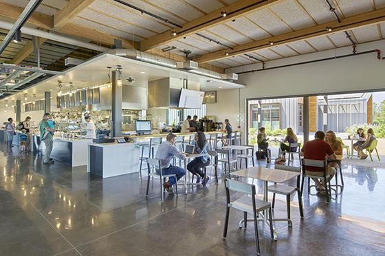 图为波胆网站伊甸大厅食堂, 一个大的工业空间，自然光线充足，桌子旁坐满了人