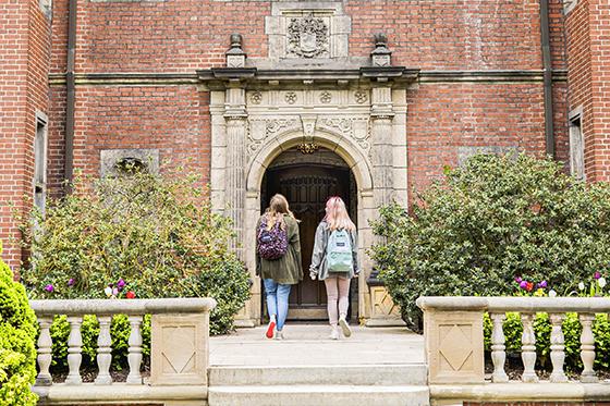 图为两名英国波胆网站女学生背着双肩包走进Shadyside校区的红砖建筑